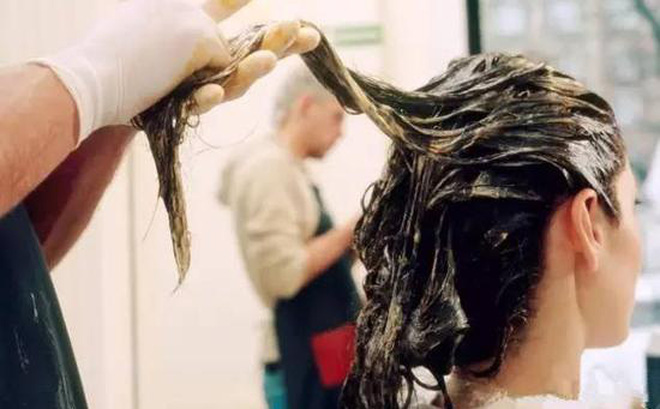 Thợ làm tóc đang phủ dầu dưỡng tóc để chuản bị cho quá trính hấp dầu phục hồi tóc sau khi uốn